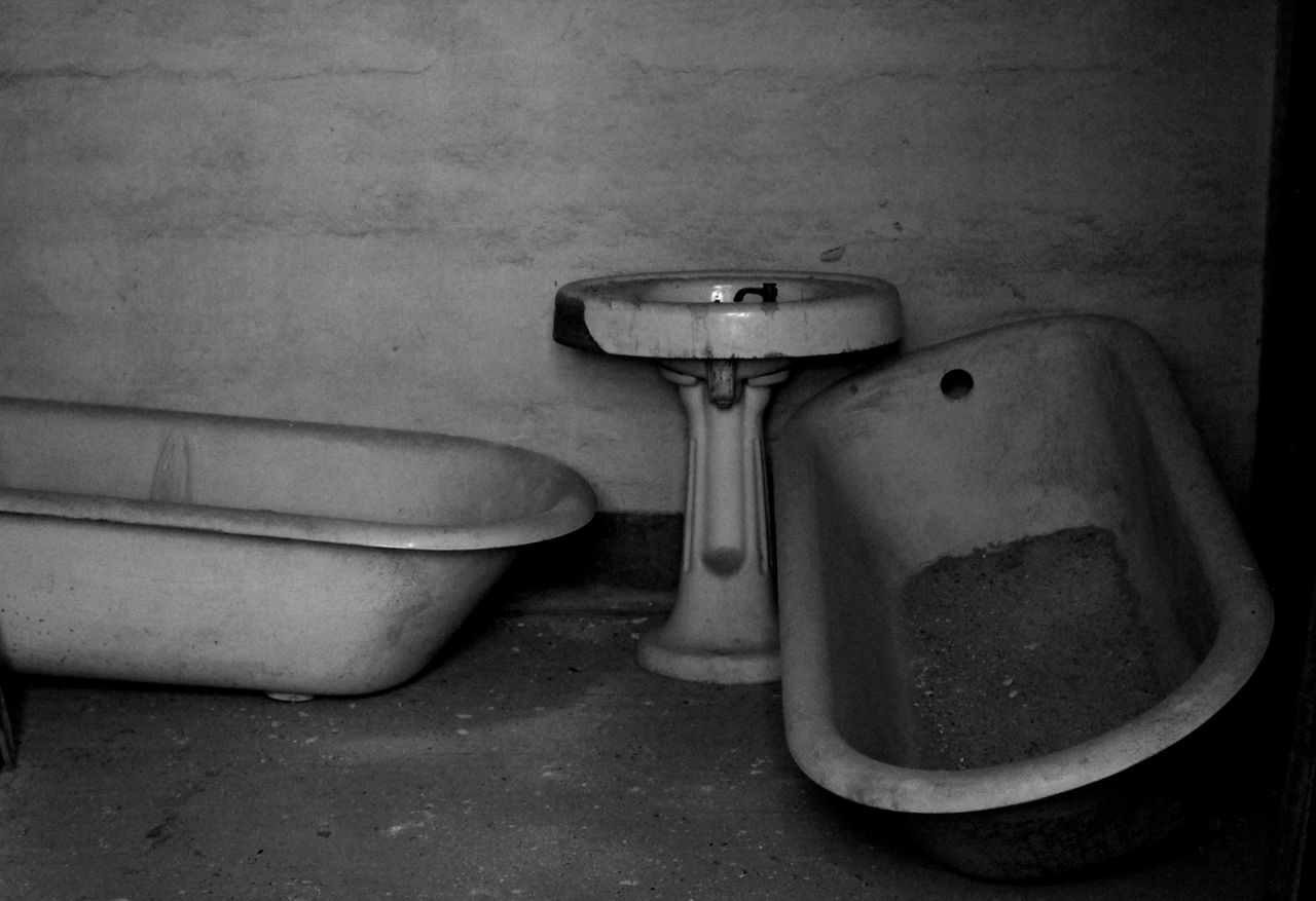 A moody black and white photo of an old, abandoned bathroom with a classic bathtub and sink.